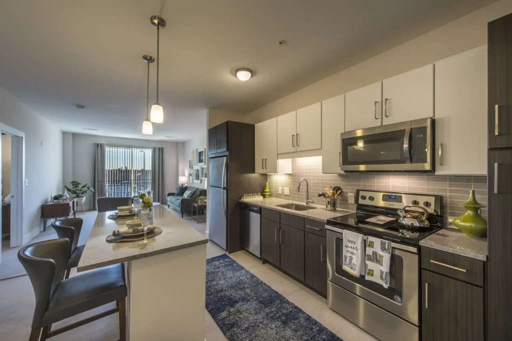 Open kitchen with view into the living room. Granite counters, stainless steel appliances, tile backsplash, island seating