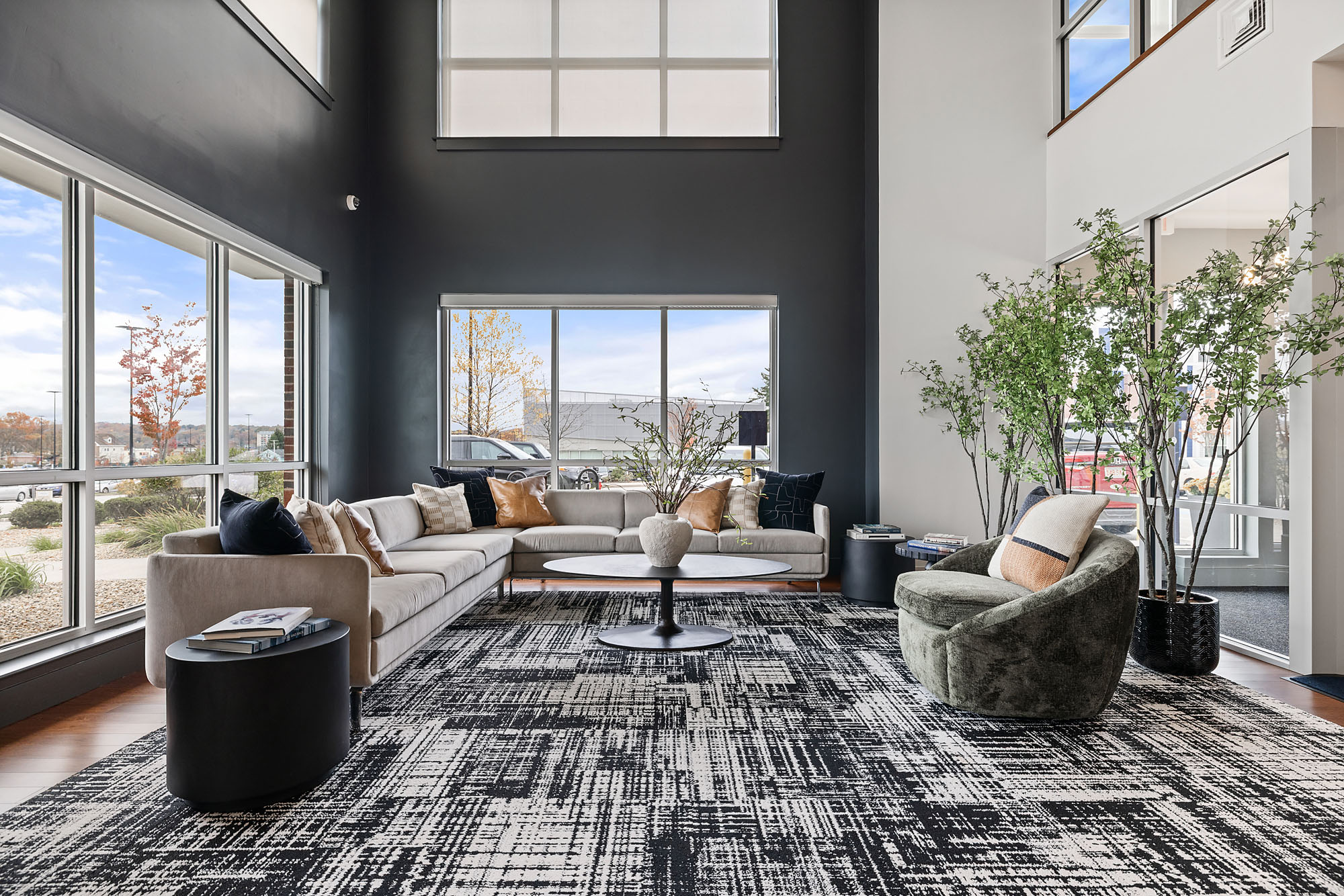 A modern Littleton CO living room with tall ceilings, large windows, neutral furniture, a black and white patterned rug, marble coffee table, and green plants, all flooded with natural light from outside.