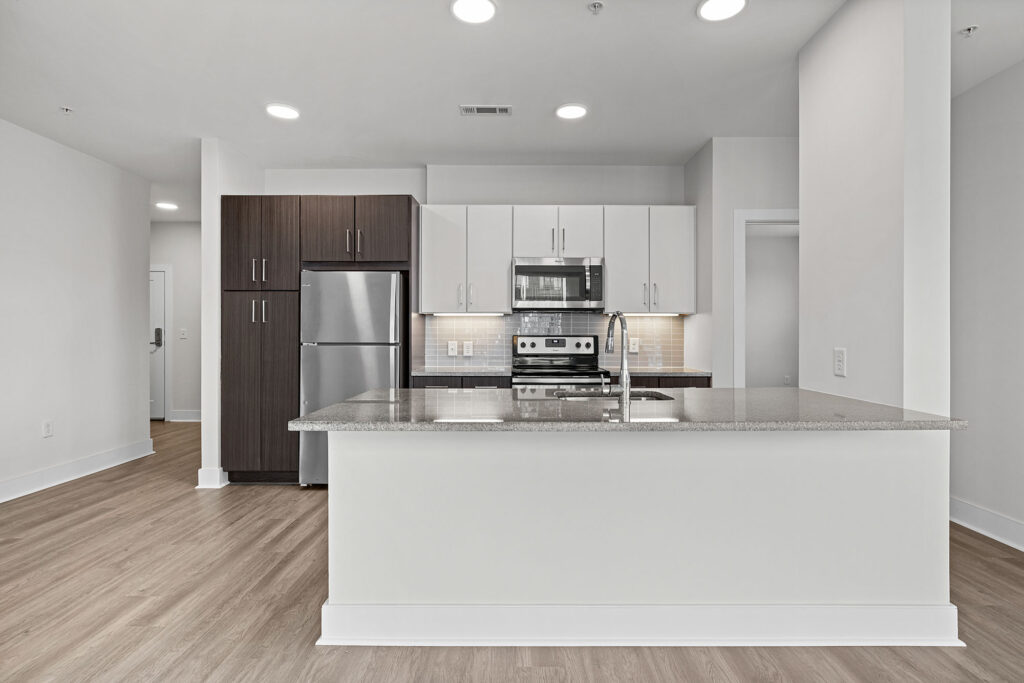 Modern kitchen with stainless steel appliances, dark brown and white cabinets, granite countertop island, light wood flooring, and neutral walls under recessed lighting.